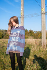 Person wearing a striped sweater with 'LET ME NO' text in a field