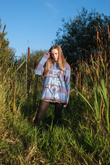 Person wearing a colorful oversized sweatshirt in a natural setting with tall grass and trees.