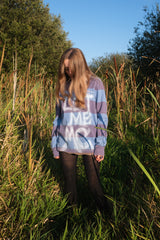 Person wearing a colorful oversized sweatshirt in a grassy field with trees in the background
