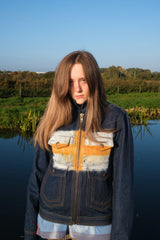 Person wearing a colorful jacket standing by a body of water with trees in the background