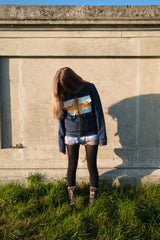 Person standing in front of a stone wall with a scenic print on their denim jacket.