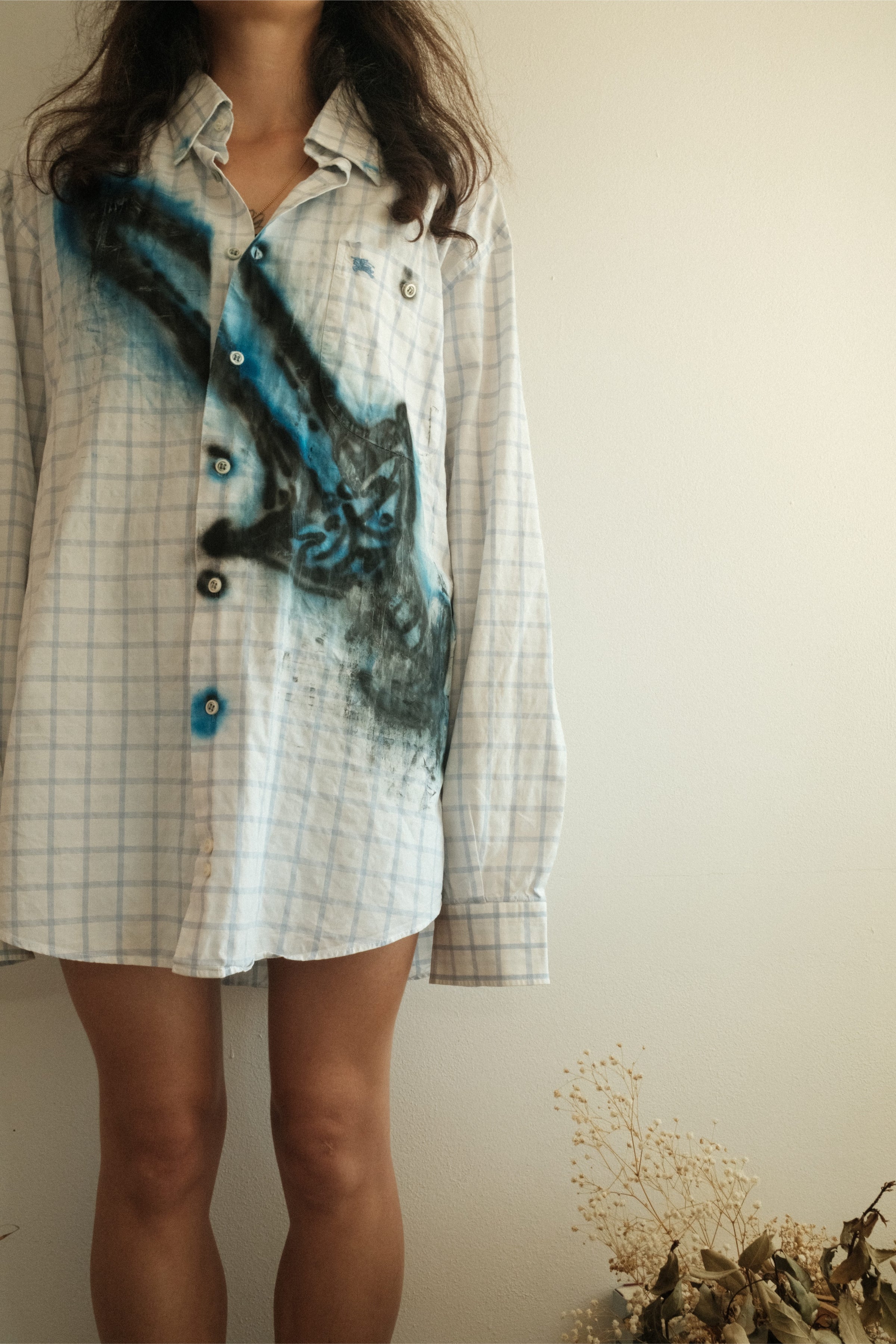 Close-up of white check shirt with abstract blue spray-painted detail, Bewept Bag of Man.