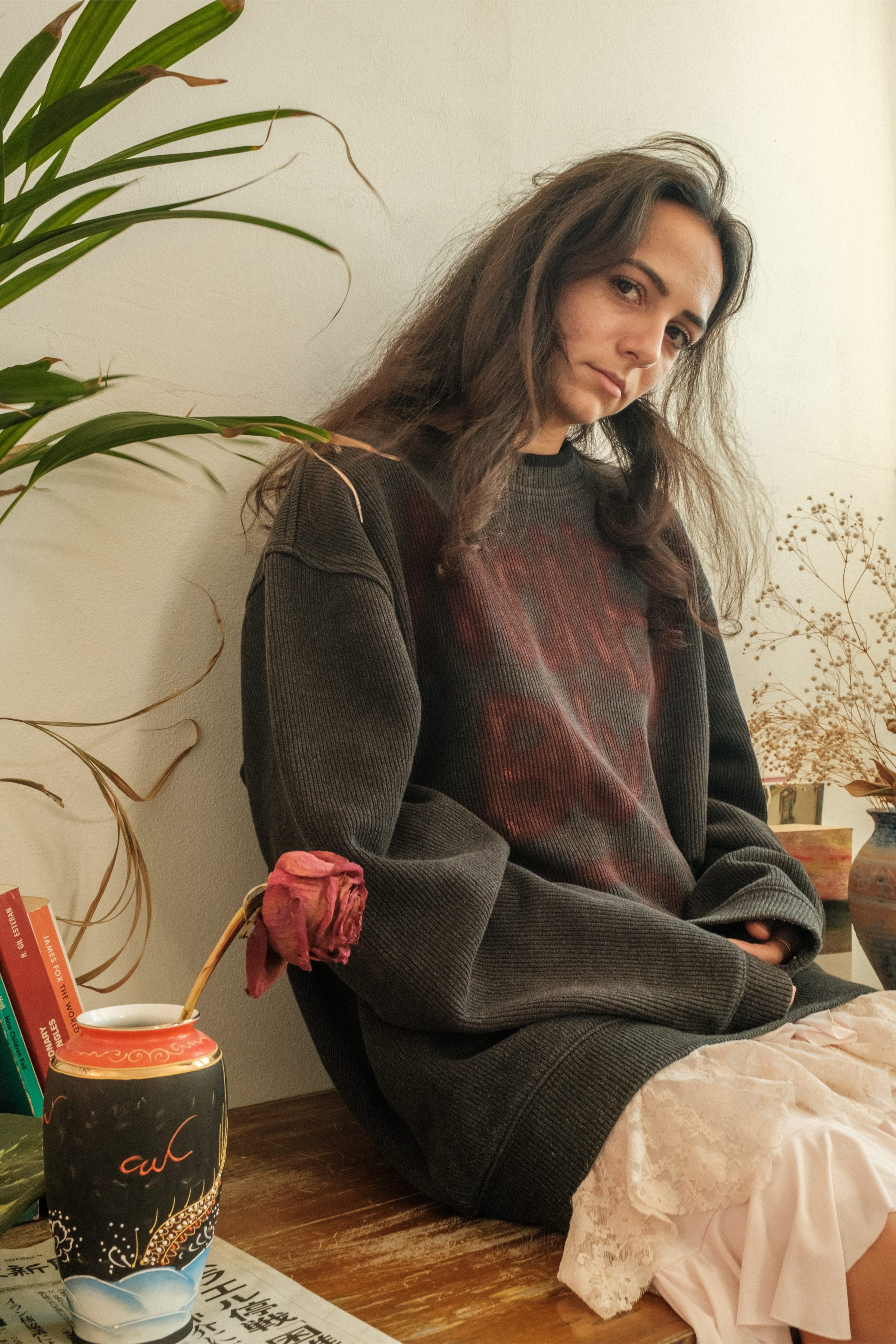 Model seated indoors wearing dark oversized sweater with red faded text, Bewept Bag of Man.