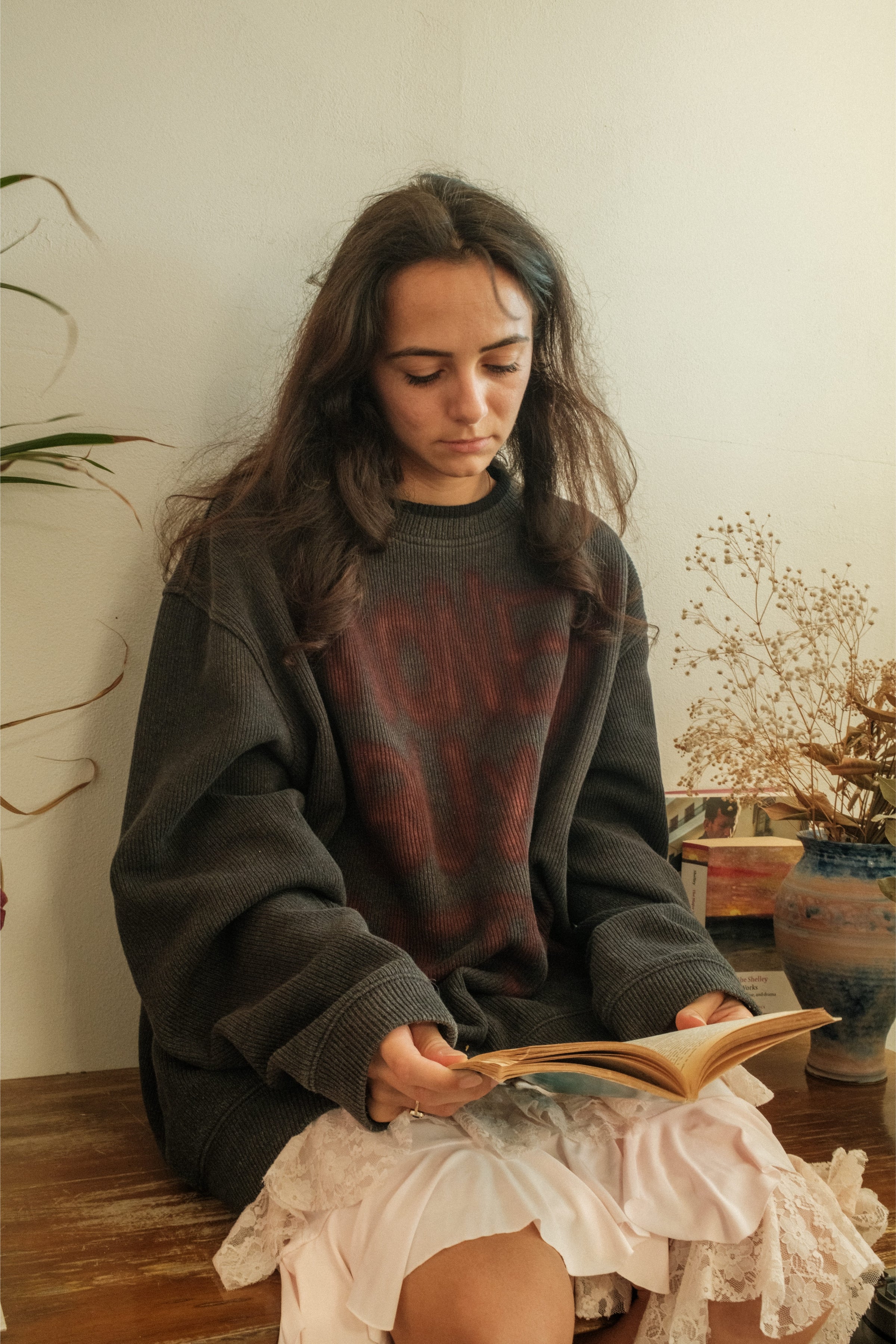 Model reading indoors wearing oversized dark sweater with red lettering, Bewept Bag of Man collection