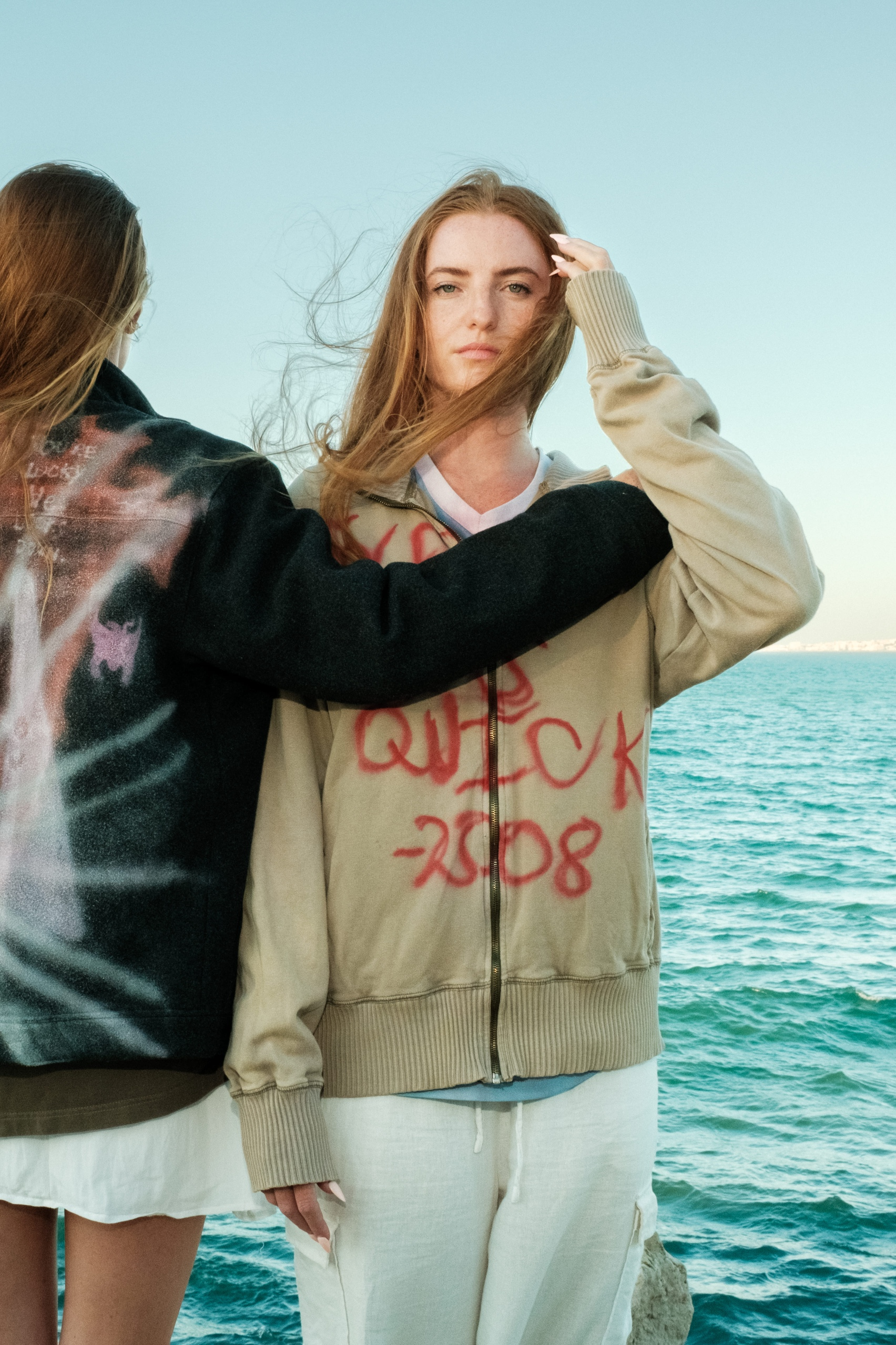 Graffiti-style beige hoodie with red spray text, styled against ocean backdrop, Bewept Bag of Man